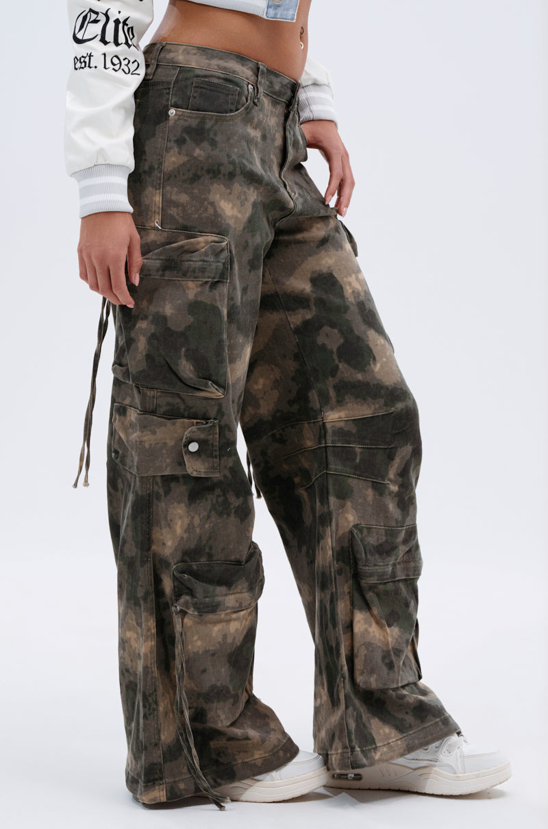 A person wearing DOWN AND DIRTY CARGO PANT in a high-rise relaxed fit camo style with multiple large pockets and white sneakers, cropped from the shoulders down against a plain white background. 4