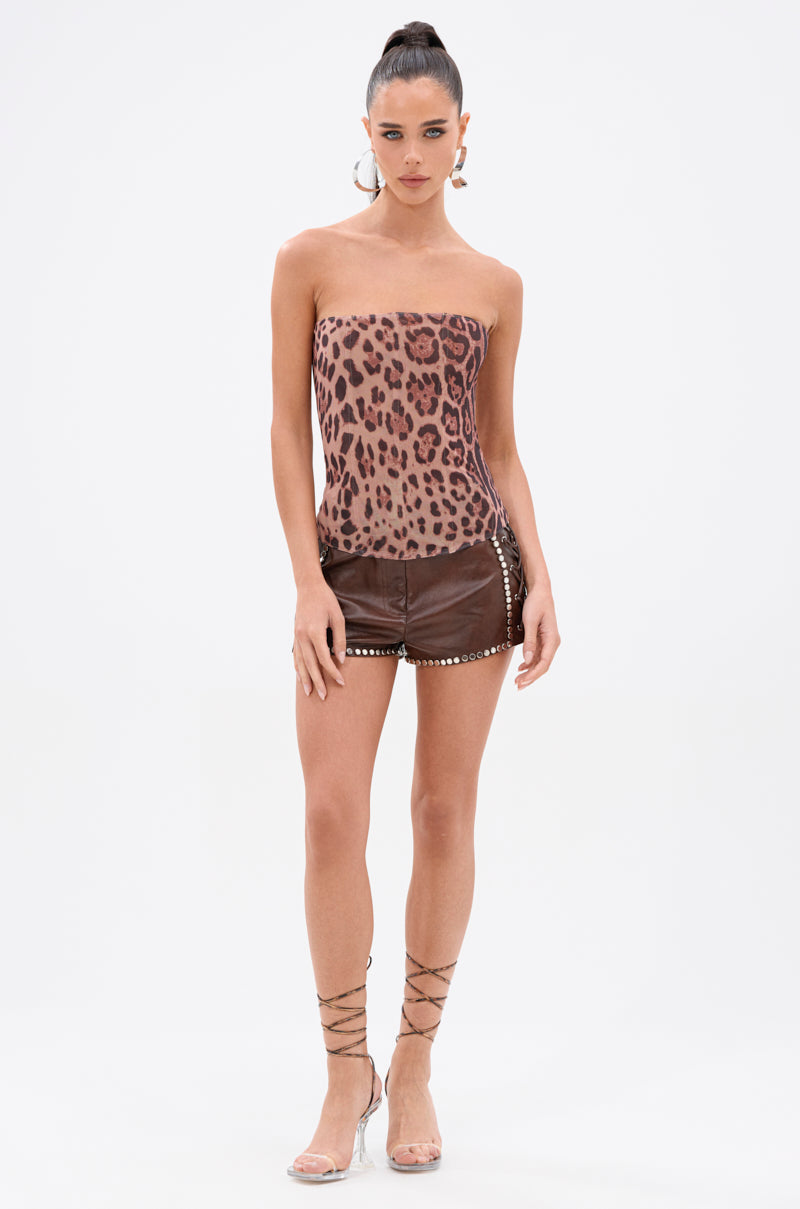 A woman poses against a white background wearing the JULIE FAUX LEATHER STUD SHORT paired with a strapless leopard-print top, clear high-heeled sandals, and hoop earrings. Her hair is styled in a high ponytail. 6