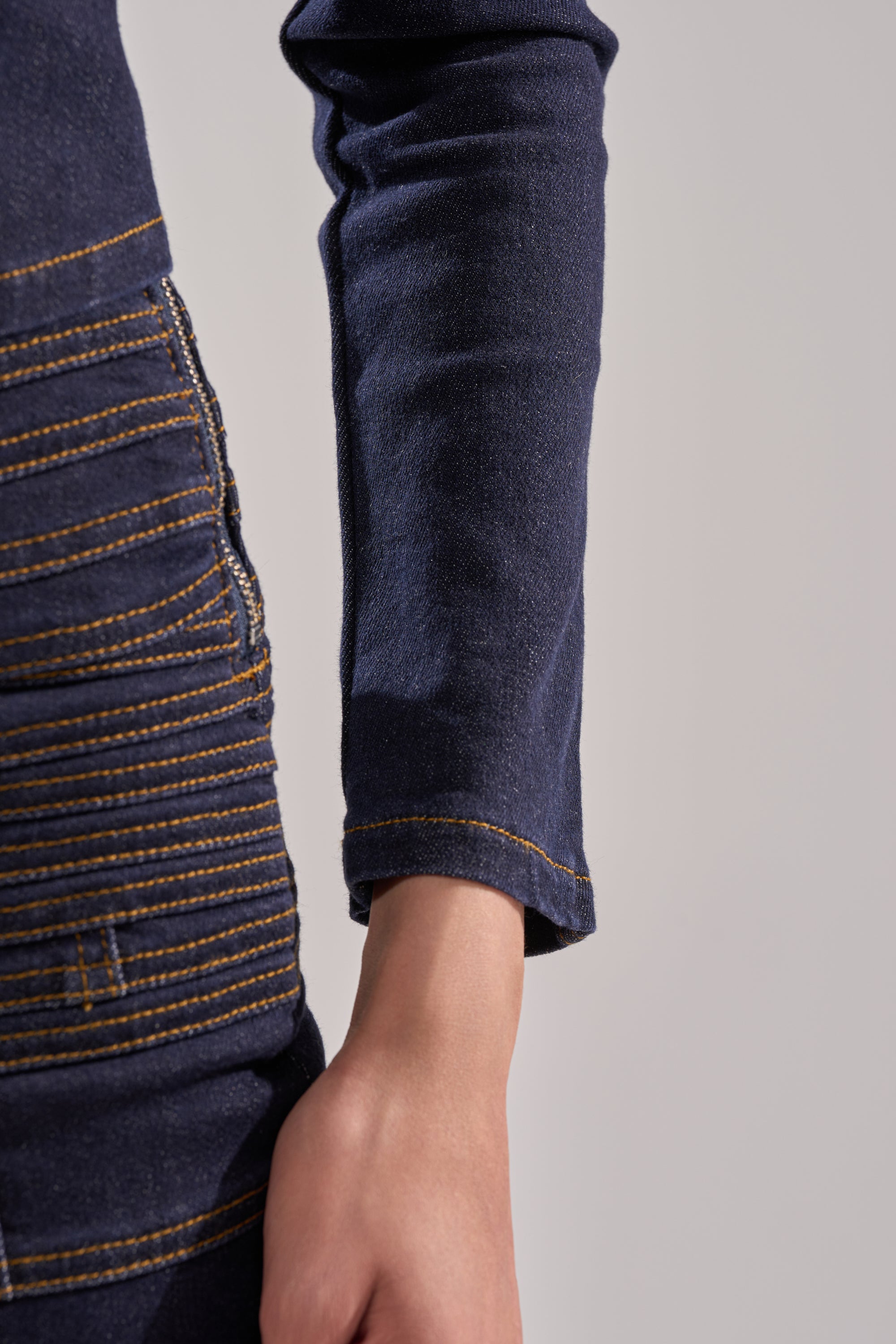A close-up of a person’s arm and hand wearing the ALL ABOUT THAT DENIM BLOUSE in dark-wash denim with visible yellow stitching, set against a plain light background. 8