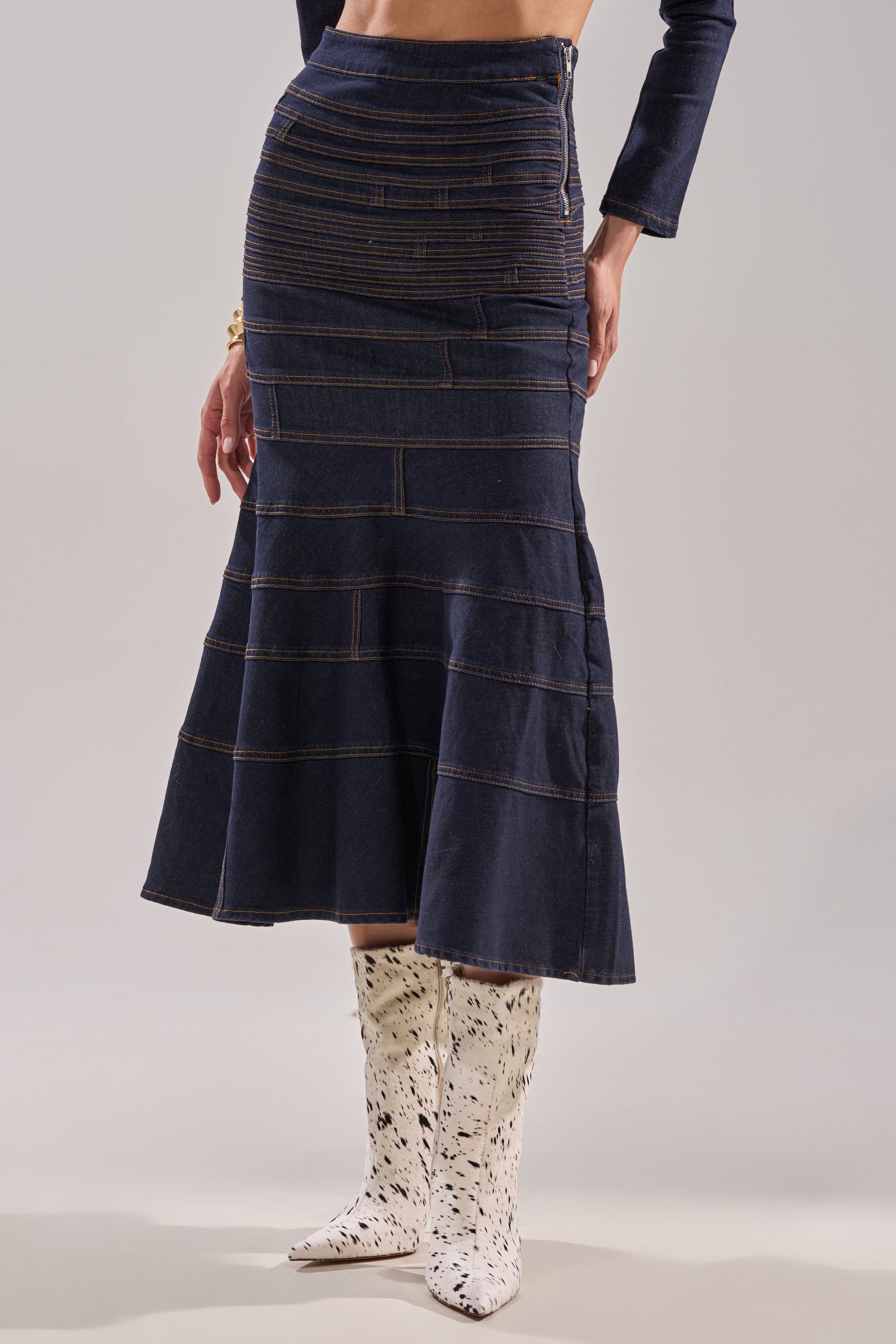Wearing the ALL ABOUT THAT DENIM MAXI SKIRT—a high-waisted, dark-wash denim maxi with horizontal stitching—a person pairs it with a long-sleeve top and white patterned cowboy boots, standing against a plain background. 1