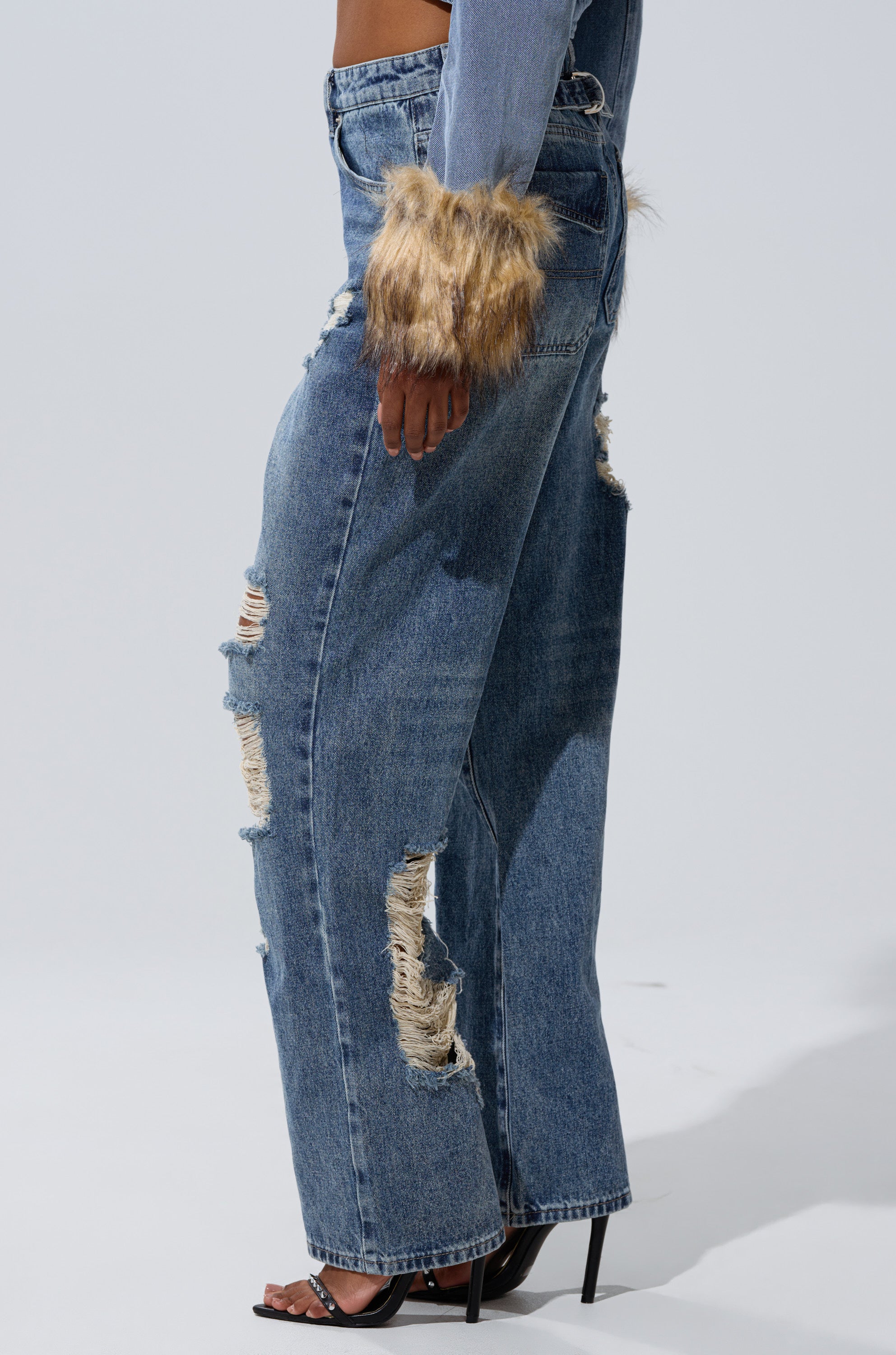 Wearing EASILY DISTRESSED DENIM wide-leg jeans and a denim jacket with faux fur cuffs, styled with high-heeled sandals, set against a plain light background.