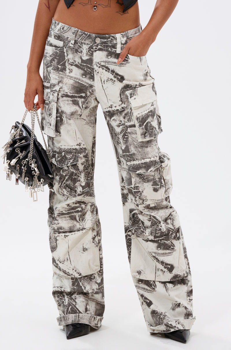 Someone wearing ASH OMBRE CARGO DENIM—loose-fitting cargo pants with a black and white abstract pattern and multiple pockets—paired with a small black handbag with keychain charms and pointed black shoes. 1