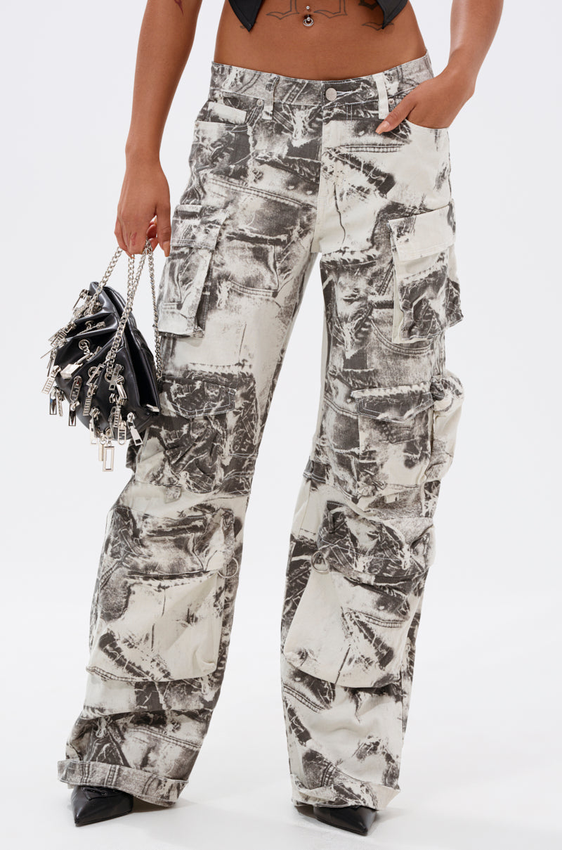 A person wearing ASH OMBRE CARGO DENIM—loose, high-waisted cargo pants with a black and white abstract pattern—paired with a small black purse featuring silver charms and black pointed-toe shoes. 2
