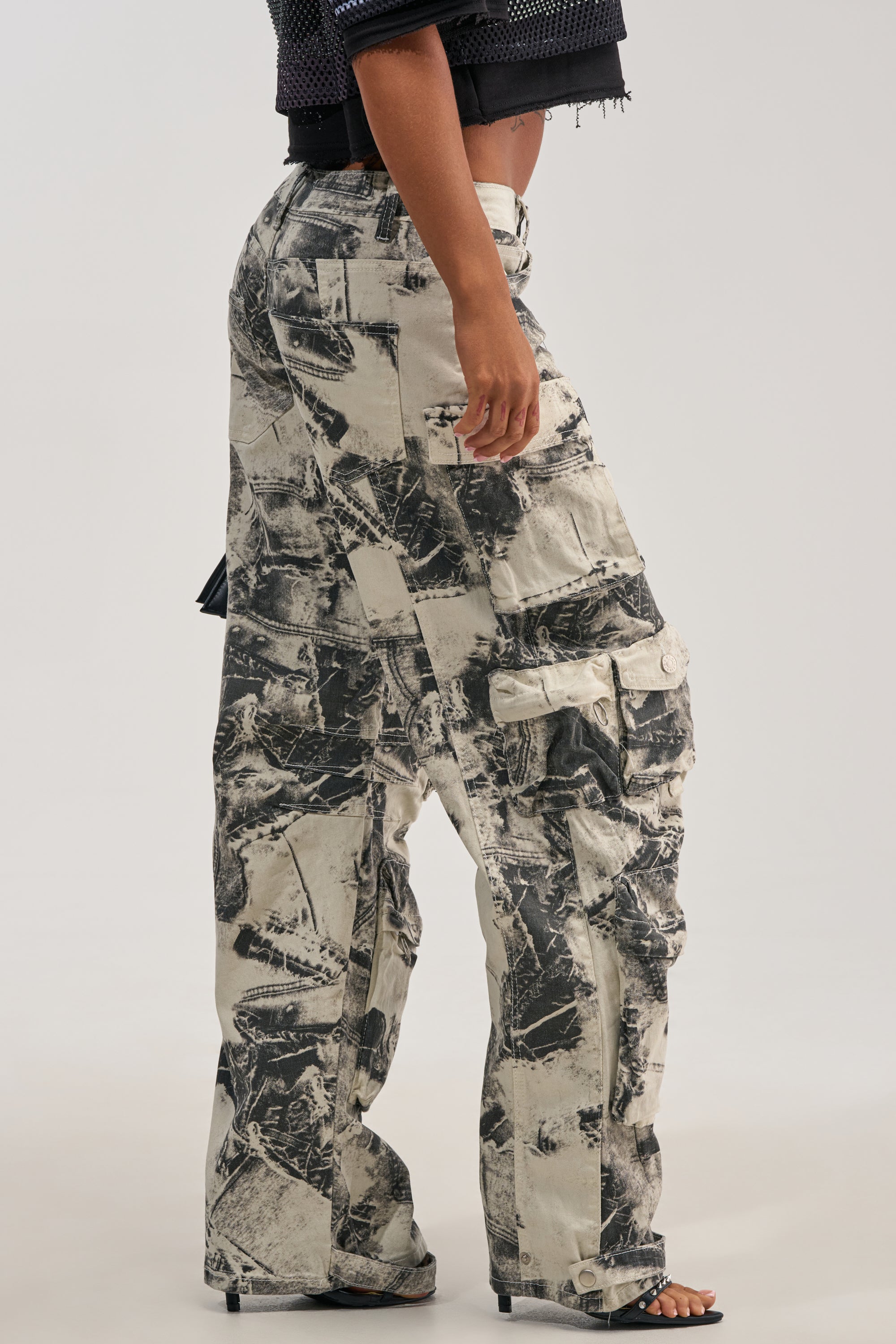 A person wearing the ASH OMBRE CARGO DENIM, high-waisted loose-fit streetwear pants featuring a black and white abstract print, paired with a cropped black textured top and open-toed heels.