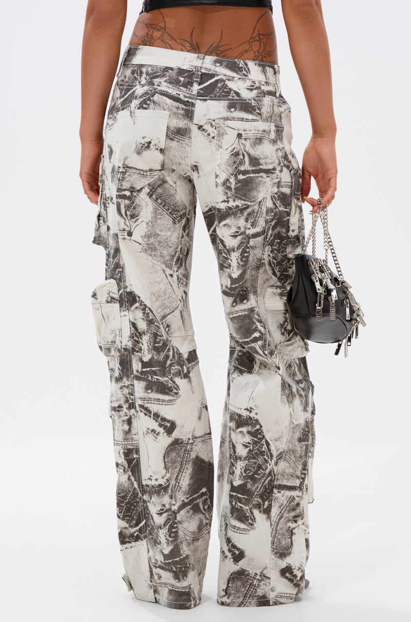 A person stands facing away, wearing ASH OMBRE CARGO DENIM—high-waisted, loose-fitting cargo jeans with a black and white abstract pattern—and holds a small black handbag with silver chains. A back tattoo peeks above the pants. 4