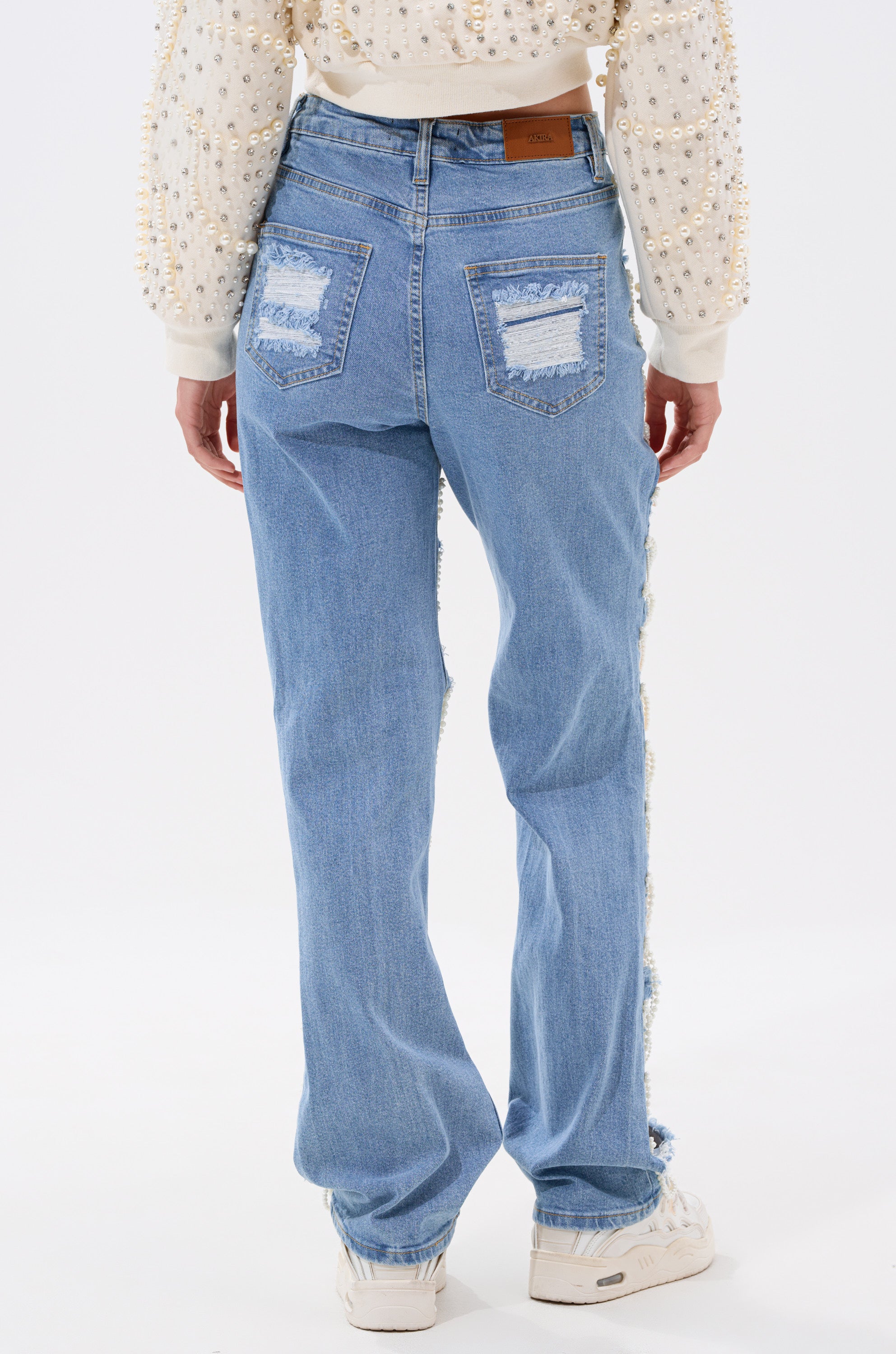 A person wearing the DISTRESSED LIFE DENIM PANT styled with faux pearl chains.