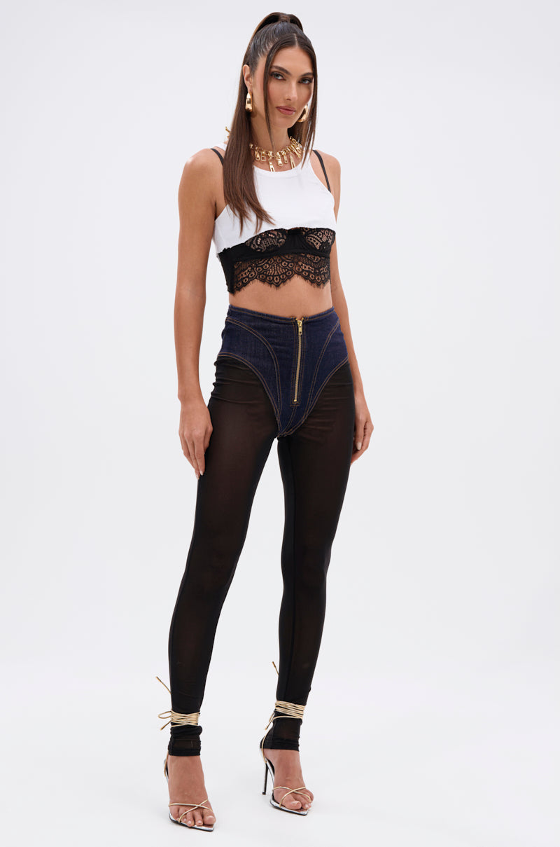 A woman poses in the ZIP ME UP MESH LEGGING WITH DENIM PANTY—a white crop top with black lace trim, high-waisted denim panty shorts with a front zipper, sheer mesh leggings—styled with gold anklets and clear heels against a white background. 8