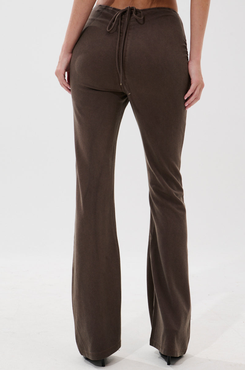 A person wearing FESTIVAL LOW RISE RUCHED FLARE LEGGING in brown, featuring ruched flare legs and a back drawstring, stands against a plain white background.