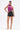 A woman stands confidently in a shiny magenta halter top, gold accessories, and the SET IT OFF FAUX LEATHER SHORT IN BLACK with gold high-heeled sandals featuring chunky chain details, posed against a white background.