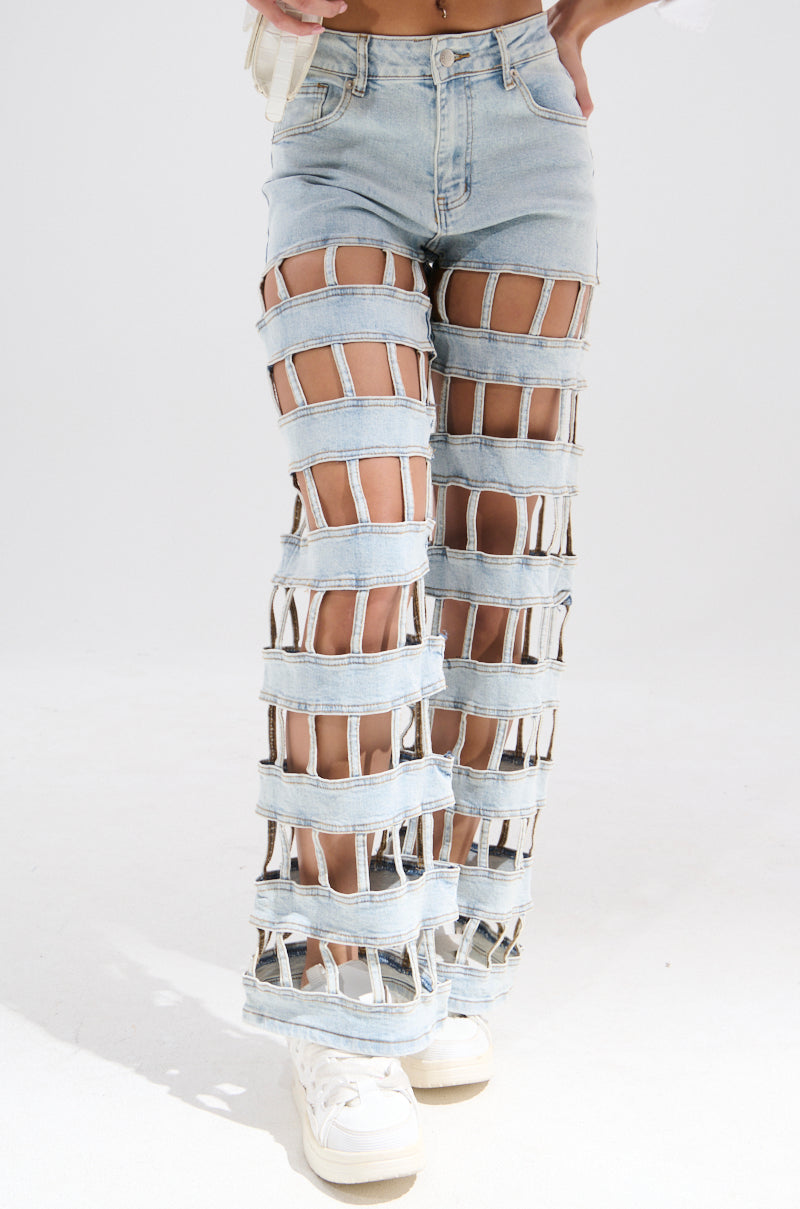 Someone models the CAGED WIDE LEG DENIM—light blue jeans with large horizontal cutouts and denim strips forming a grid pattern. The cropped, wide-leg style is paired with white sneakers, set against a plain background.