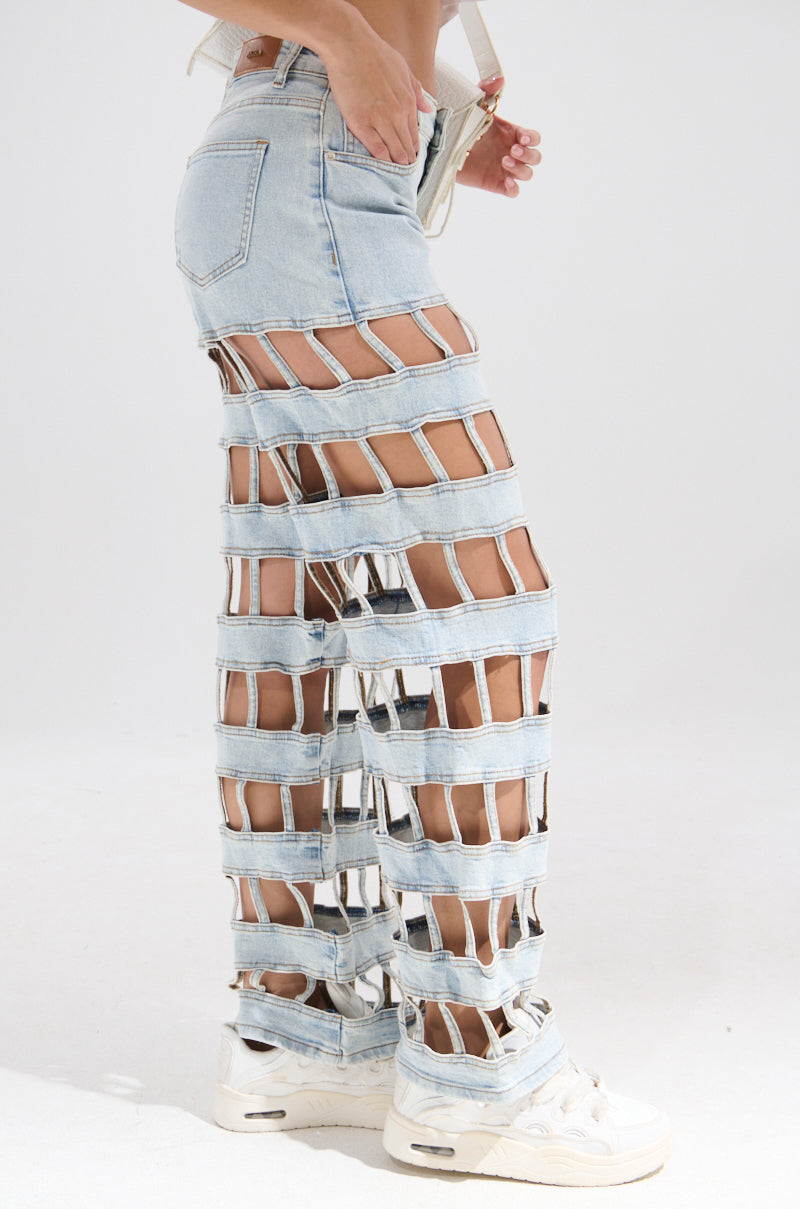 Model wears light blue CAGED WIDE LEG DENIM with high-rise fit and bold horizontal cutouts, paired with white shoes and posed against a plain white background.
