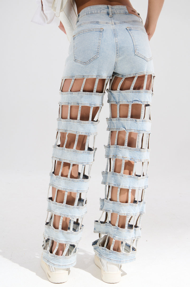 Wearing CAGED WIDE LEG DENIM, featuring light blue wide-leg jeans with large horizontal cutouts from waist to ankle for a bold, grid-like pattern. These high-rise jeans make a striking statement as the wearer faces away from the camera.