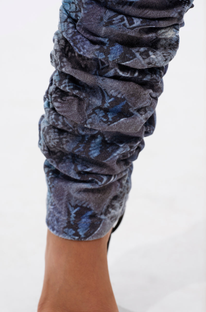 A close-up of a person's lower leg wearing DAYS END RUCHED STACKED SNAKE SKINNY DENIM, barefoot on a light surface. 5