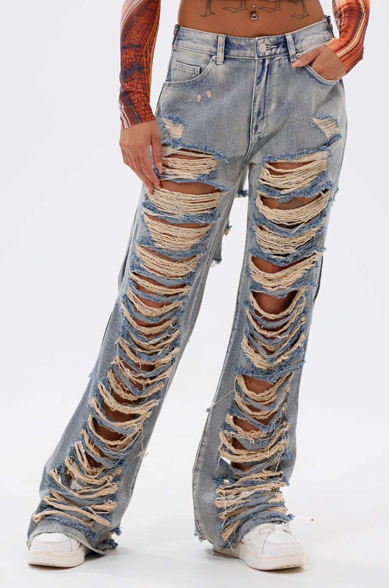 Someone wearing the REAL TALK DISTRESSED JEANS, featuring light blue vintage wash and bold horizontal rips exposing much of the legs, paired with white sneakers and a long-sleeve fitted top. 1