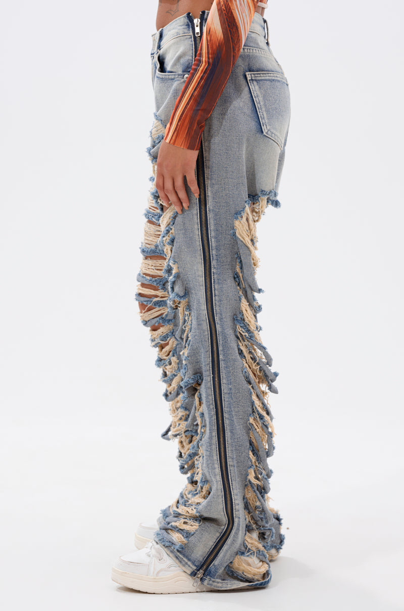 A person wears the REAL TALK DISTRESSED JEANS—light blue, high-rise, straight-leg denim with frayed edges and side zippers—paired with a brown long-sleeve top and white sneakers, standing against a plain white background. 2