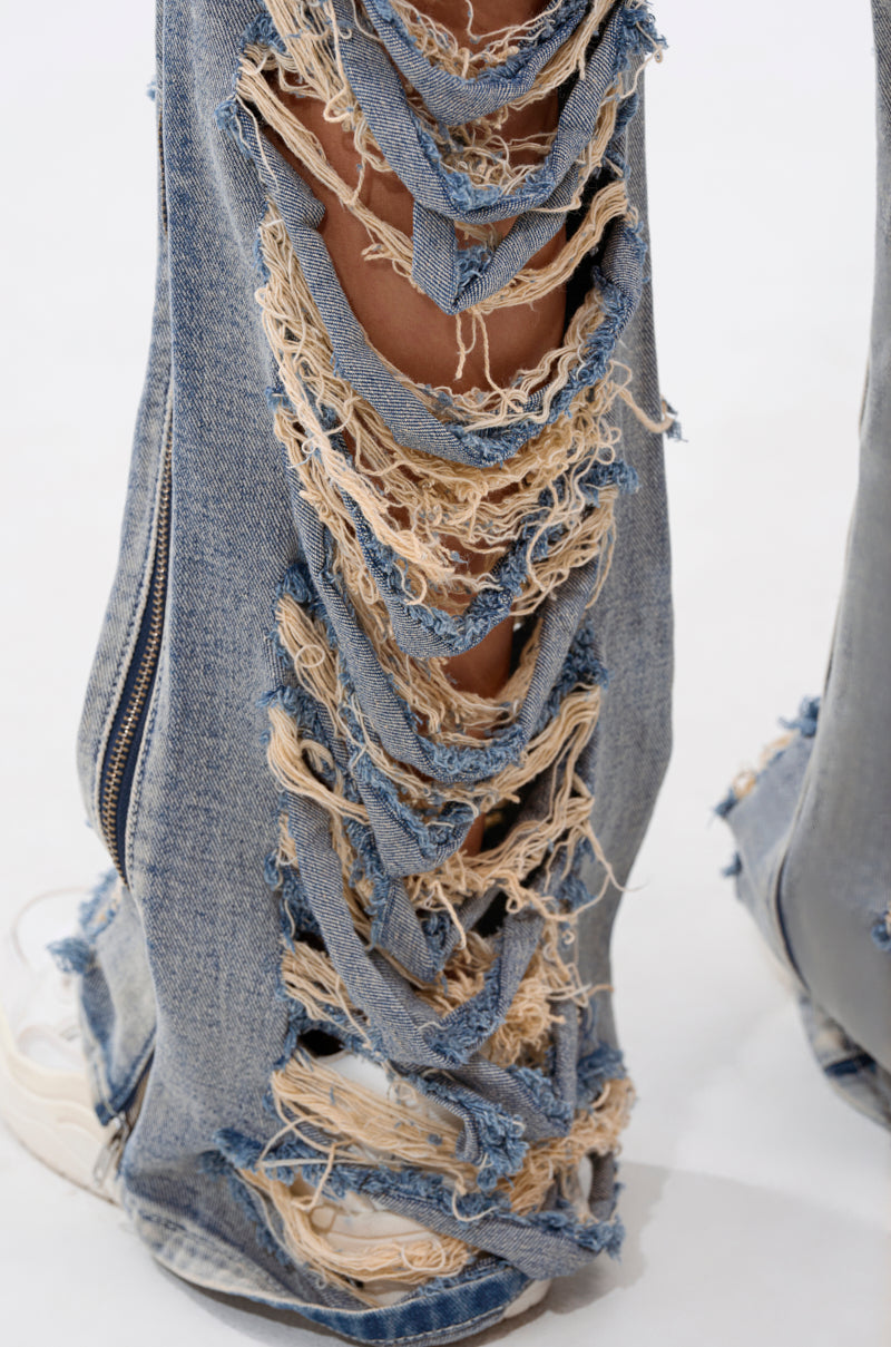 Close-up of the REAL TALK DISTRESSED JEANS: high-rise straight-leg, light blue vintage-wash denim with large rips and frayed edges. Paired with white sneakers, zipper detail visible on the side. 6