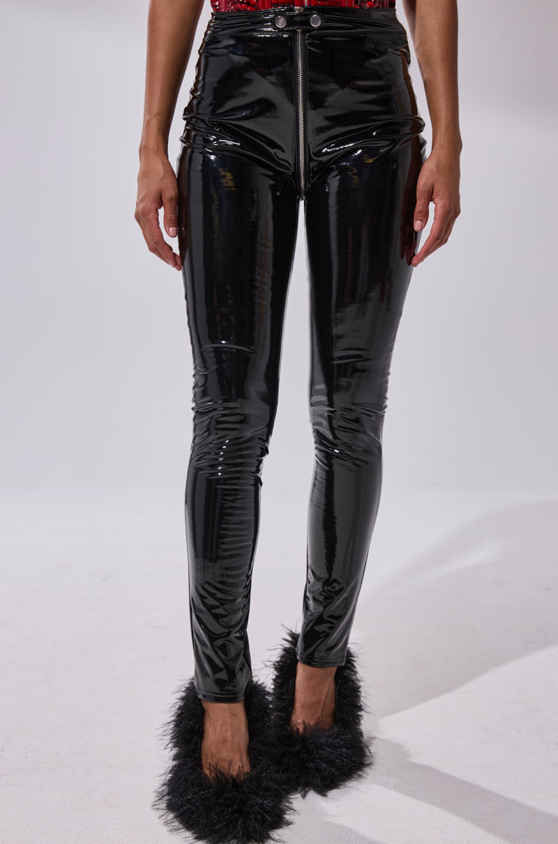 A person stands against a white background, wearing the DROP IT LIKE ITS HOT VINYL LEGGING WITH ZIPPER and black high-heeled shoes with fluffy trim. Only their lower body is visible.