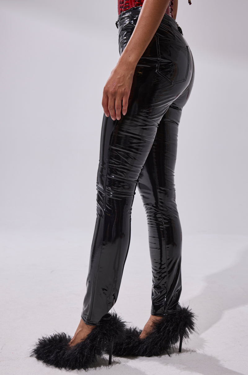 A person wearing DROP IT LIKE ITS HOT VINYL LEGGING WITH ZIPPER and black high-heeled shoes with fluffy feather trim stands against a plain white background.