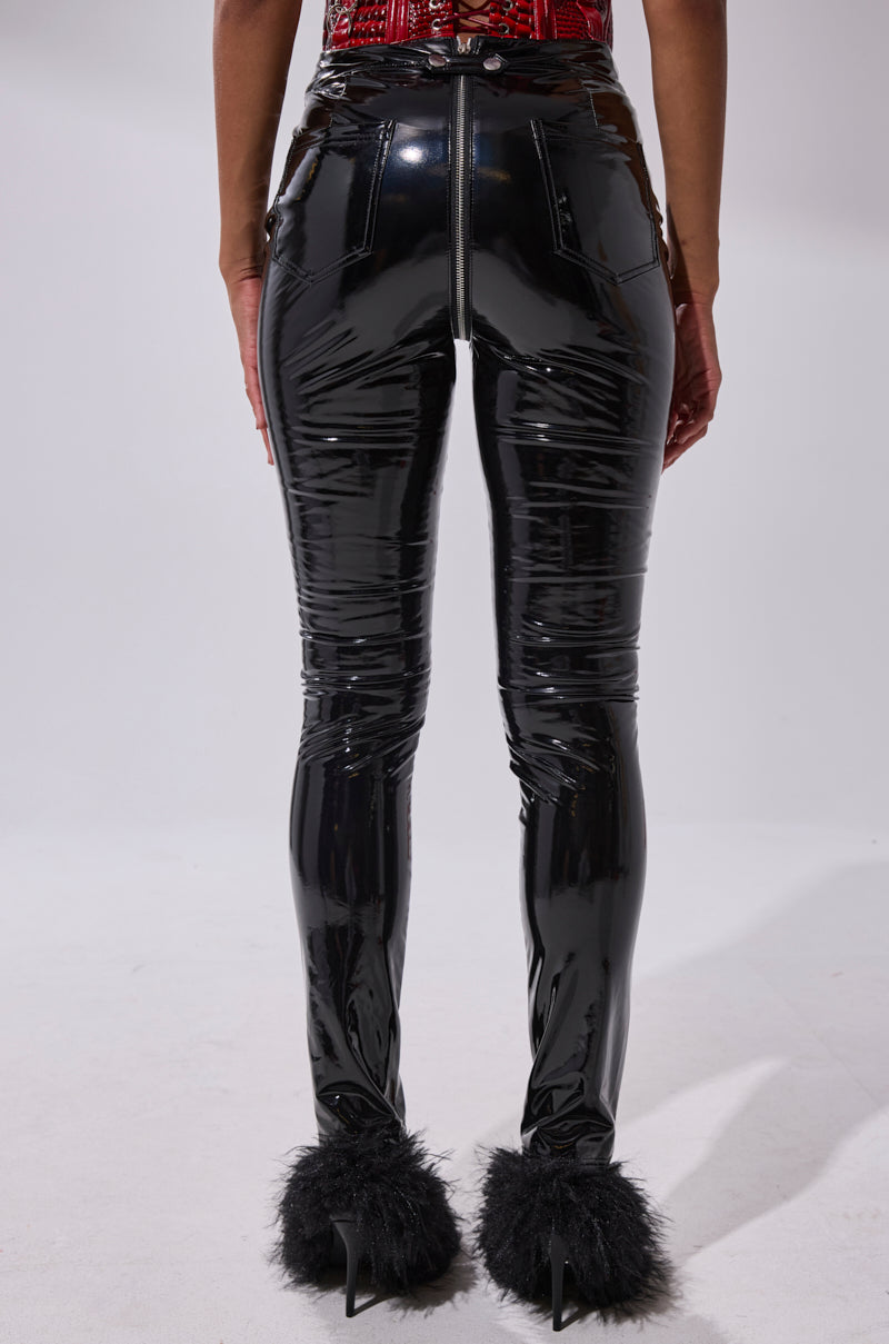 A person faces away from the camera in DROP IT LIKE ITS HOT VINYL LEGGING WITH ZIPPER, featuring a high rise and center zipper, paired with black faux fur high heels against a plain, light background.