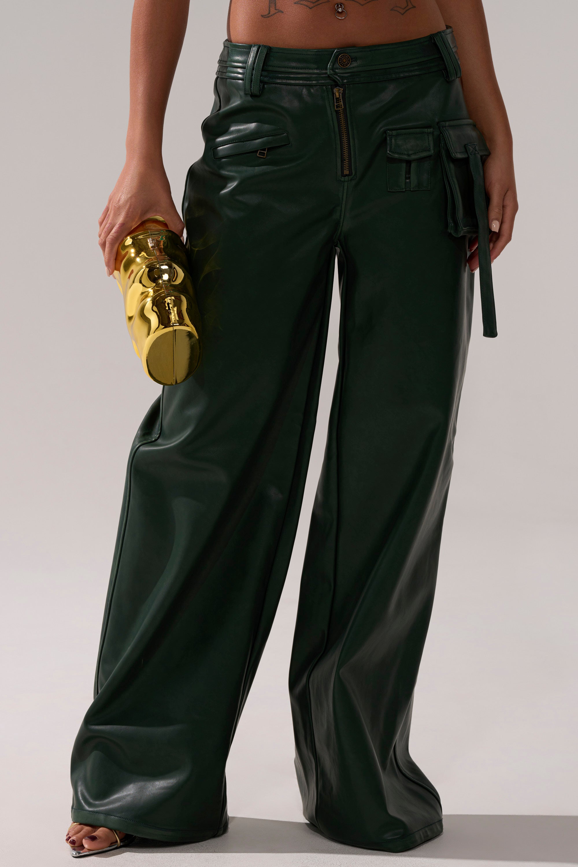 A person wears the SO YOU THOUGHT TROUSER—shiny dark green wide-leg pants with cargo pockets—while holding a metallic gold teddy bear-shaped clutch. Only the lower torso and legs are visible against a neutral background. 1