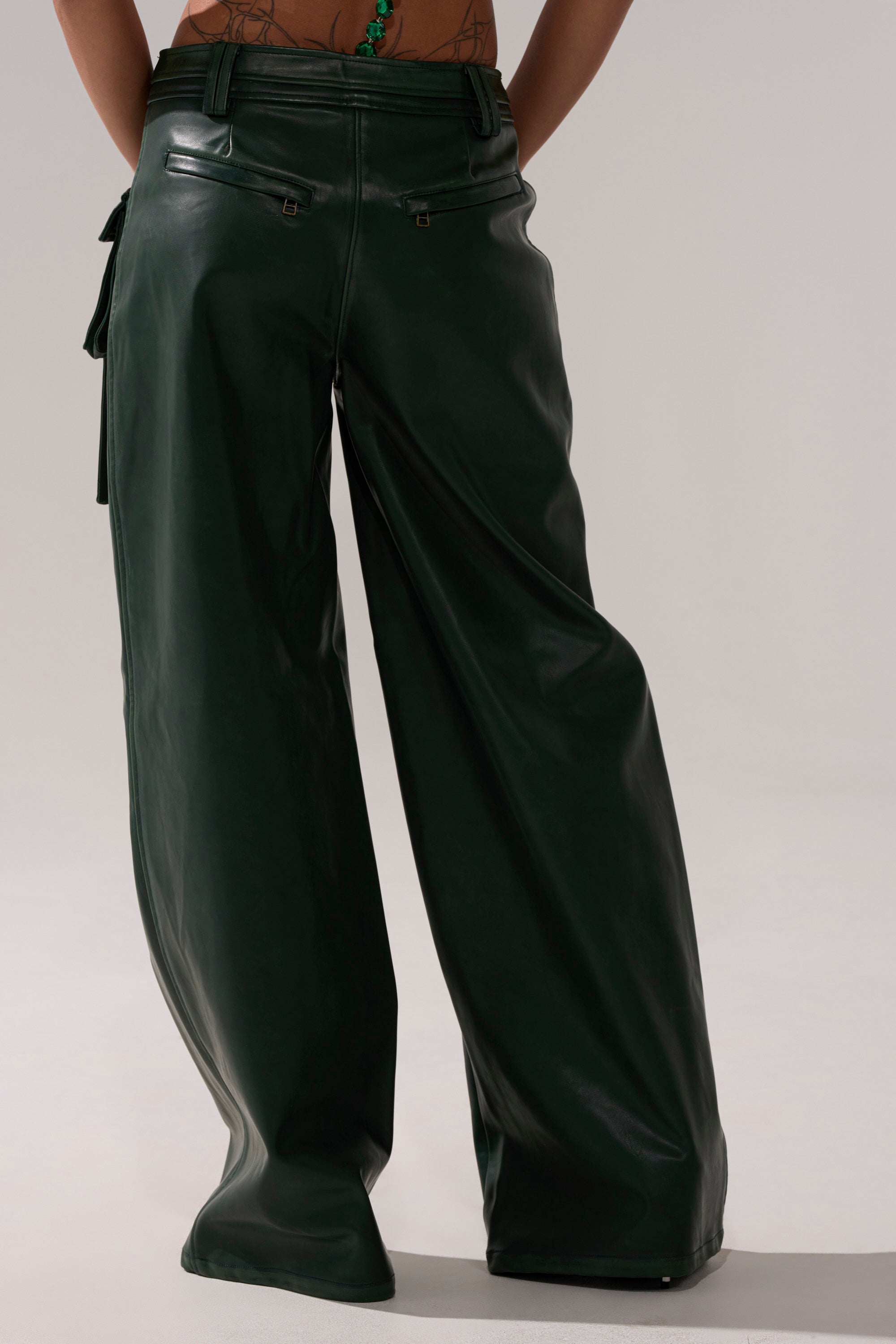 A person shown from the waist down wears SO YOU THOUGHT TROUSER—loose-fitting, dark green faux leather pants. Their lower back tattoos are visible against a plain, neutral background. 4