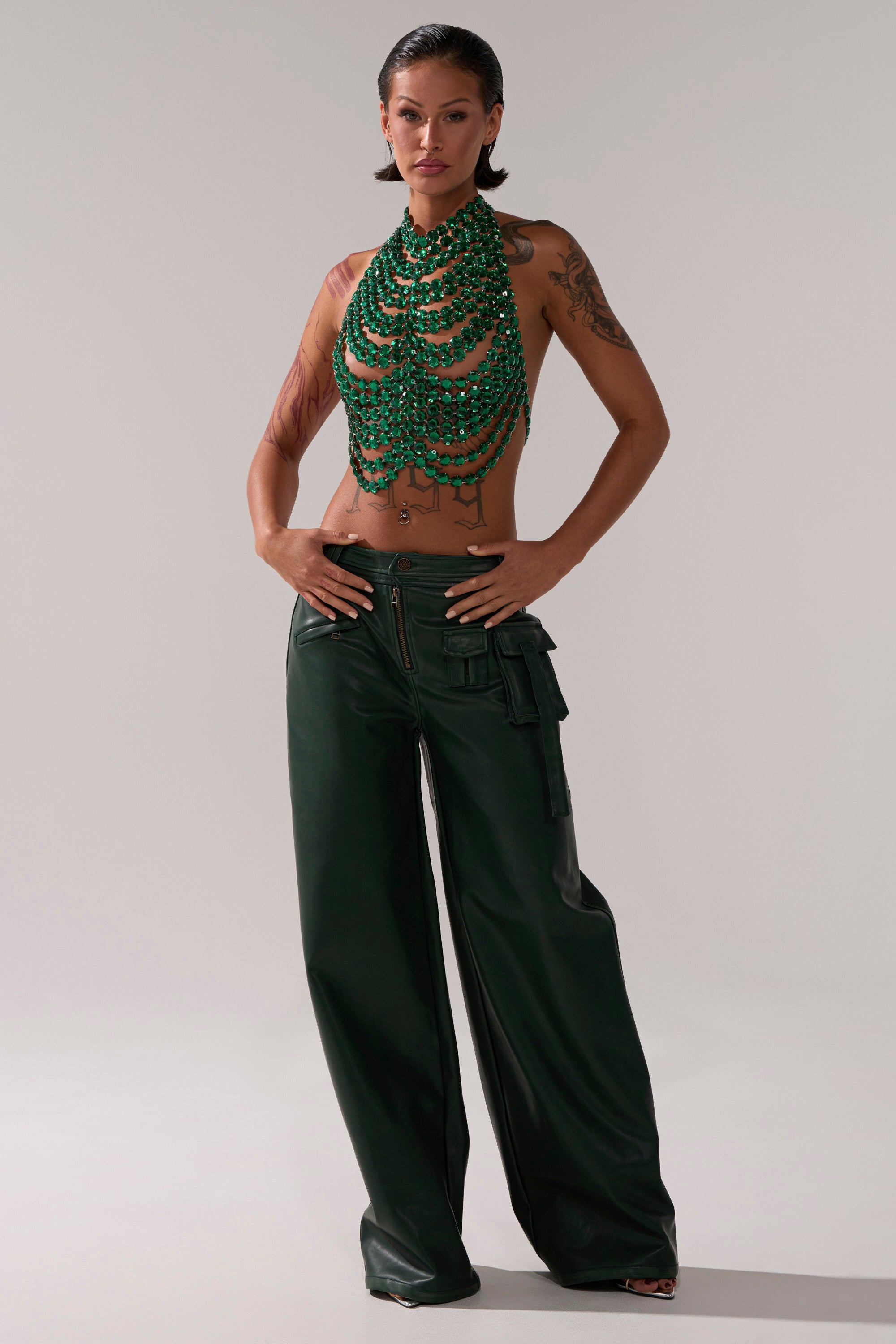 A woman poses confidently in SO YOU THOUGHT TROUSER wide-leg dark green pants with cargo pockets and a green beaded halter top, showing off her arm tattoos and wet-look hair against a plain light background. 6