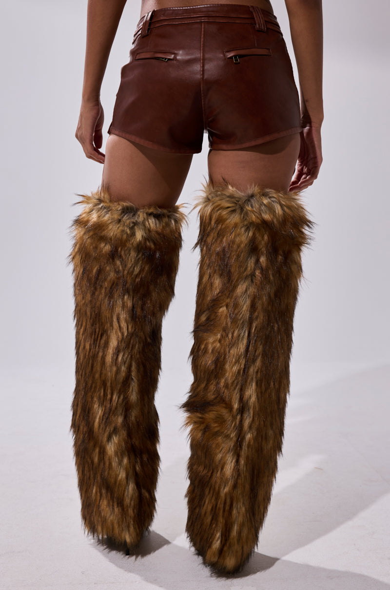 A person is standing, seen from behind, wearing mini-length NICOLETTE FAUX LEATHER SHORTS and tall, furry brown leg warmers that reach their thighs against a plain light background. 5