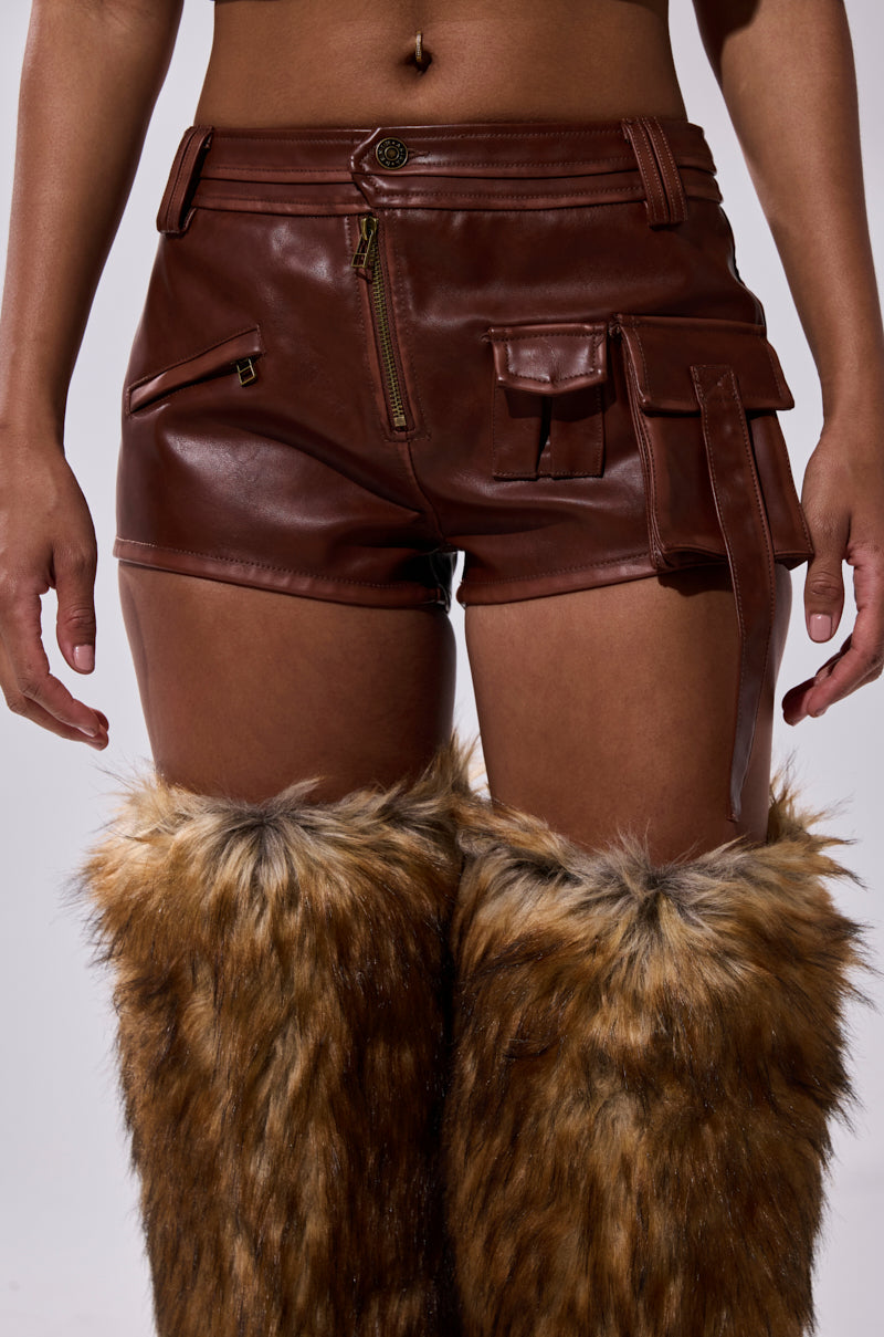 Someone wears the NICOLETTE FAUX LEATHER SHORT featuring cargo pockets and zipper details, paired with tall furry brown and tan boots. The image is cropped to show only the torso and legs. 1