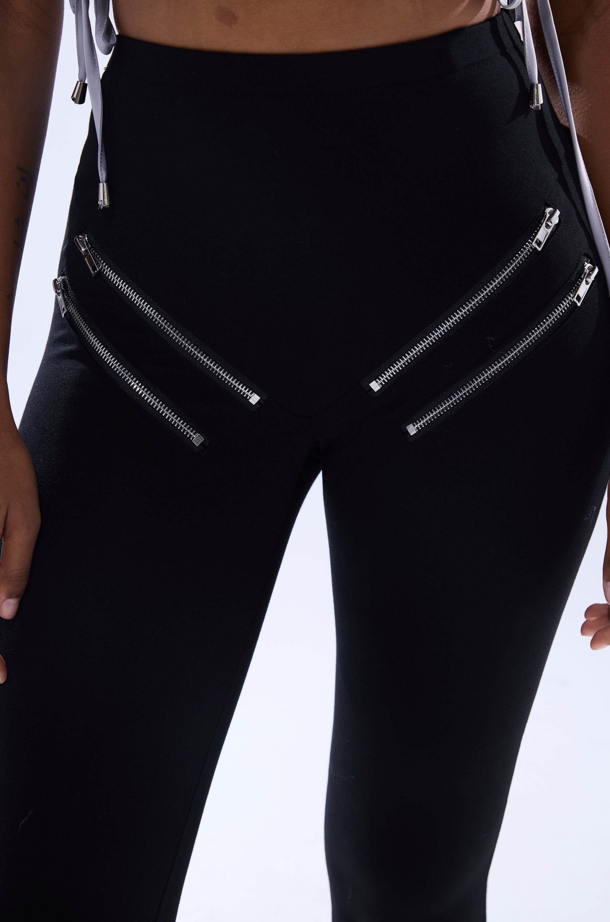 A close-up shows someone wearing the ZIP ME UP SEAMLESS LEGGING, a high-rise style with four diagonal silver zippers on the hips. Their hands and part of their torso are also visible.