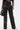 Person wearing the ROCK MY WORLD FAUX LEATHER LACE UP PANT, featuring lace-up details, mesh cutouts, and silver eyelets, paired with a matching jacket with white sleeve stripes and holding a black handbag.