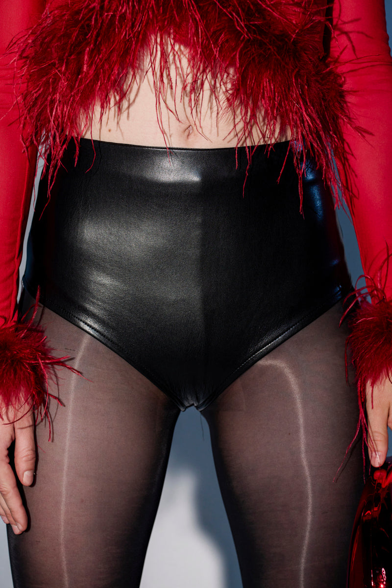 Wearing LETS PARTY HOT SHORT faux leather shorts with sheer black tights and a red feather-trimmed top, the cropped photo highlights these bold party bottoms from chest to upper thighs. 0