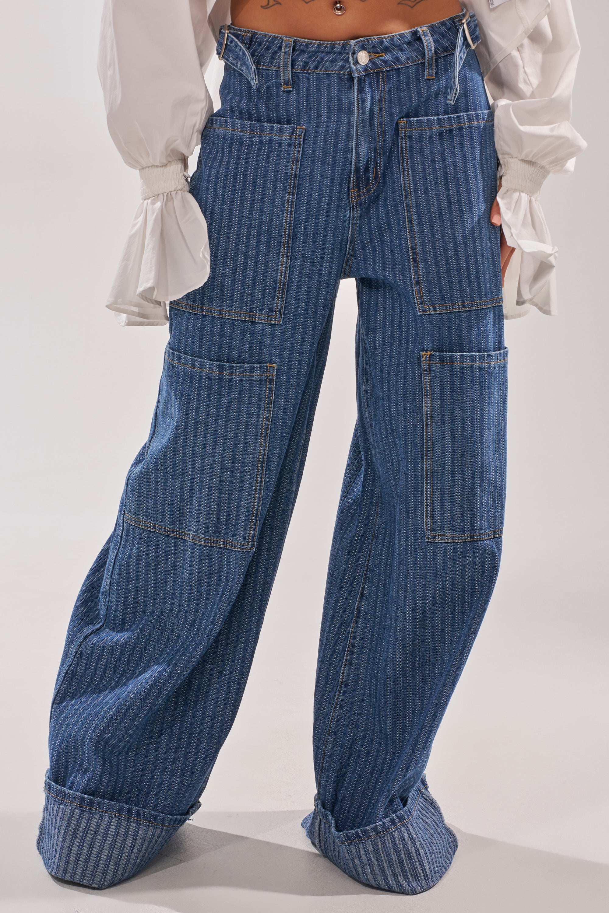 A person wears the BE MINE STRIPE DENIM—wide-leg, dark wash blue jeans with large front patch pockets and rolled cuffs—paired with a white blouse with ruffled sleeves. The image is cropped at the torso. 3