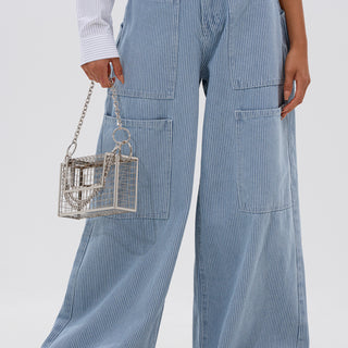 Wearing the SUMMERTIME BLUES STRIPE WIDE LEG DENIM and a white long-sleeve top, a person holds a small silver birdcage purse. Only their lower half is visible.