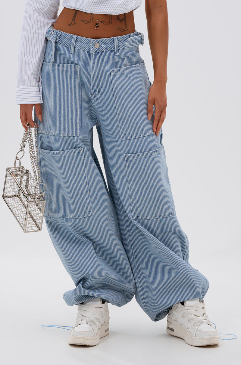 Wearing SUMMERTIME BLUES STRIPE WIDE LEG DENIM, a cropped white shirt showcasing a geometric tattoo, chunky white sneakers, and carrying a silver geometric handbag. 3