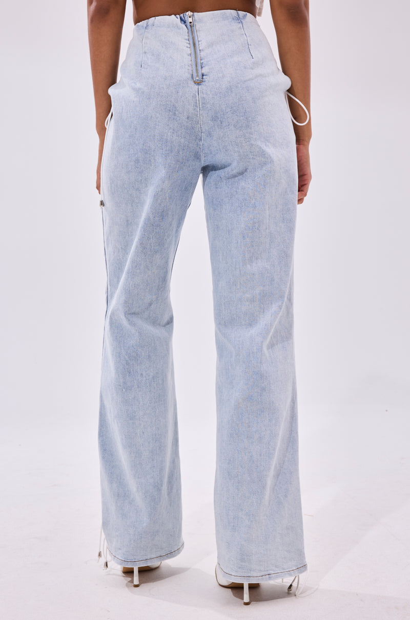 A person is shown from the back wearing FEELING BLESSED LACE UP DENIM—high waisted, wide leg jeans with zipper and seam details—paired with white heeled shoes against a plain background.