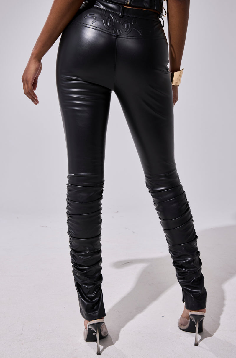 A person stands facing away, wearing the BADDIE STACKED FAUX LEATHER PANT with a skinny-leg fit, ruched detailing, and decorative waistband stitching, paired with clear heels against a plain light background. 4