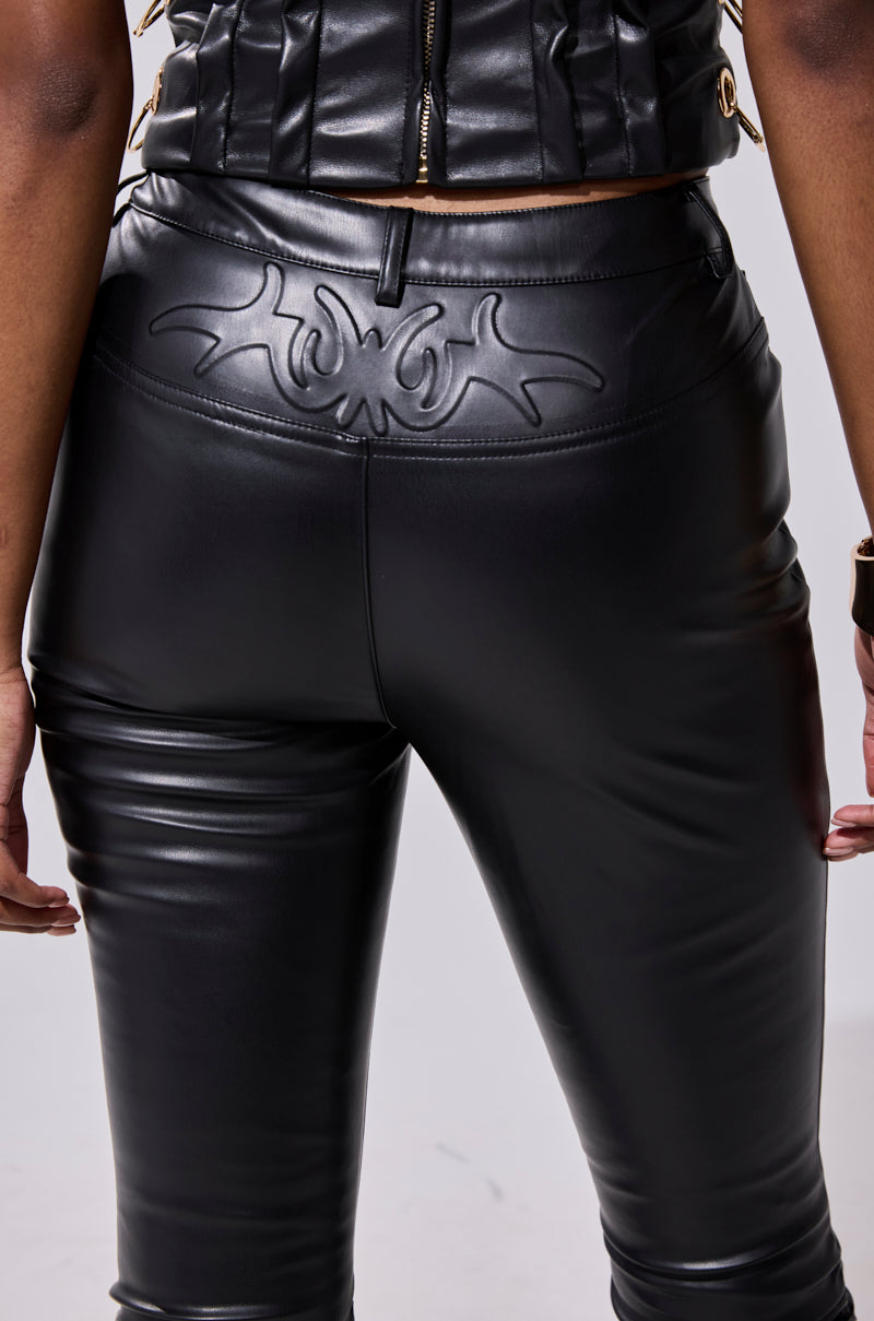 A person wears the BADDIE STACKED FAUX LEATHER PANT—high-waisted and black with an embossed abstract design on the back waistband and a skinny-leg fit—paired with a black leather top, shown from the waist down, facing away. 8
