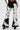 A person wears LETS GO TO THE RODEO BABY COW DENIM pants with black and white faux cowhide flared panels and a fuzzy texture, paired with black pointed-toe shoes. The upper body is mostly out of frame.