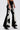 Someone wears LETS GO TO THE RODEO BABY COW DENIM—black high-rise flare jeans with white and black cow-print fuzzy panels—paired with black pointed-toe heeled shoes, set against a plain white background.