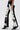 Wearing the LETS GO TO THE RODEO BABY COW DENIM—high-rise, cow print jeans with textured, fuzzy fabric—paired with black pointed-toe heels. Only the lower torso and legs appear against a plain background, highlighting the bold western style.