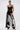 A woman poses in LETS GO TO THE RODEO BABY COW DENIM high rise flare jeans, a sheer black lace top layered over a black bra, pointed shoes, hoop earrings, and a choker necklace against a plain light background.