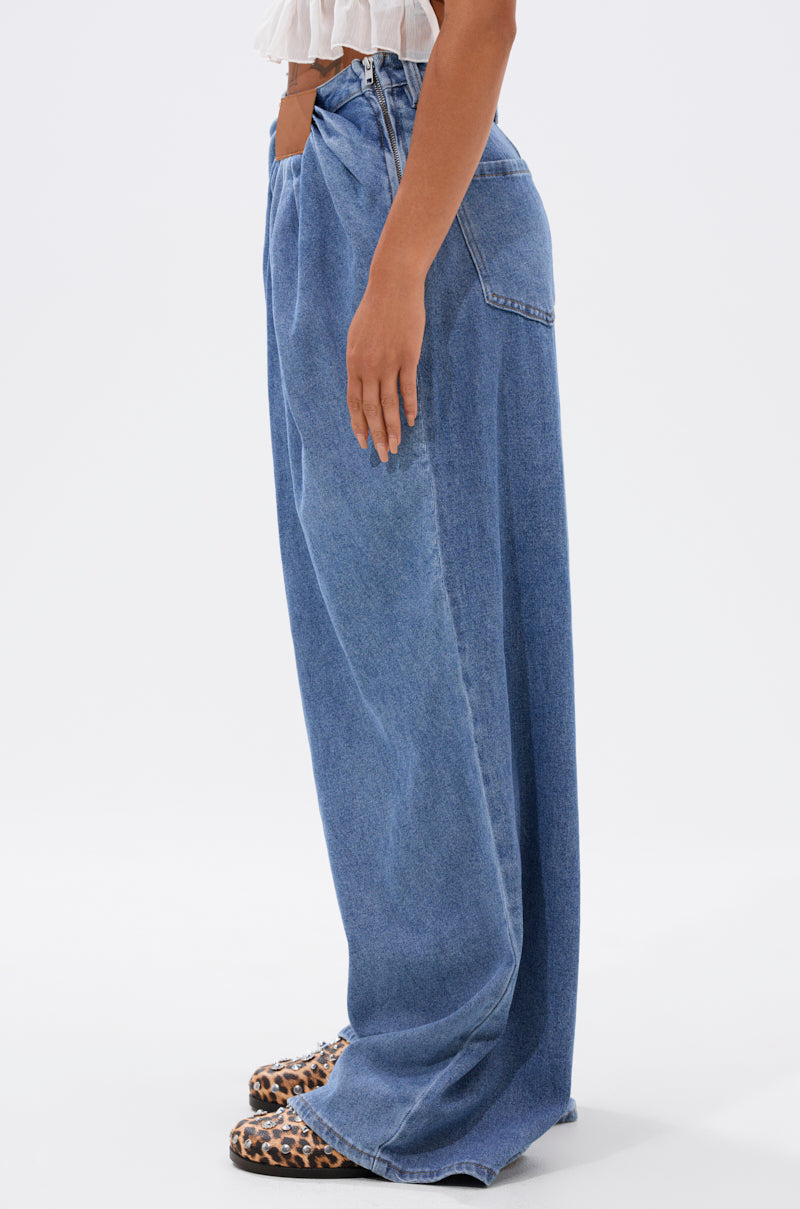 A person wearing TOO MUCH FOR YOU WIDE LEG DENIM and leopard print shoes is shown standing sideways against a plain white background, with only the lower half of their body visible.