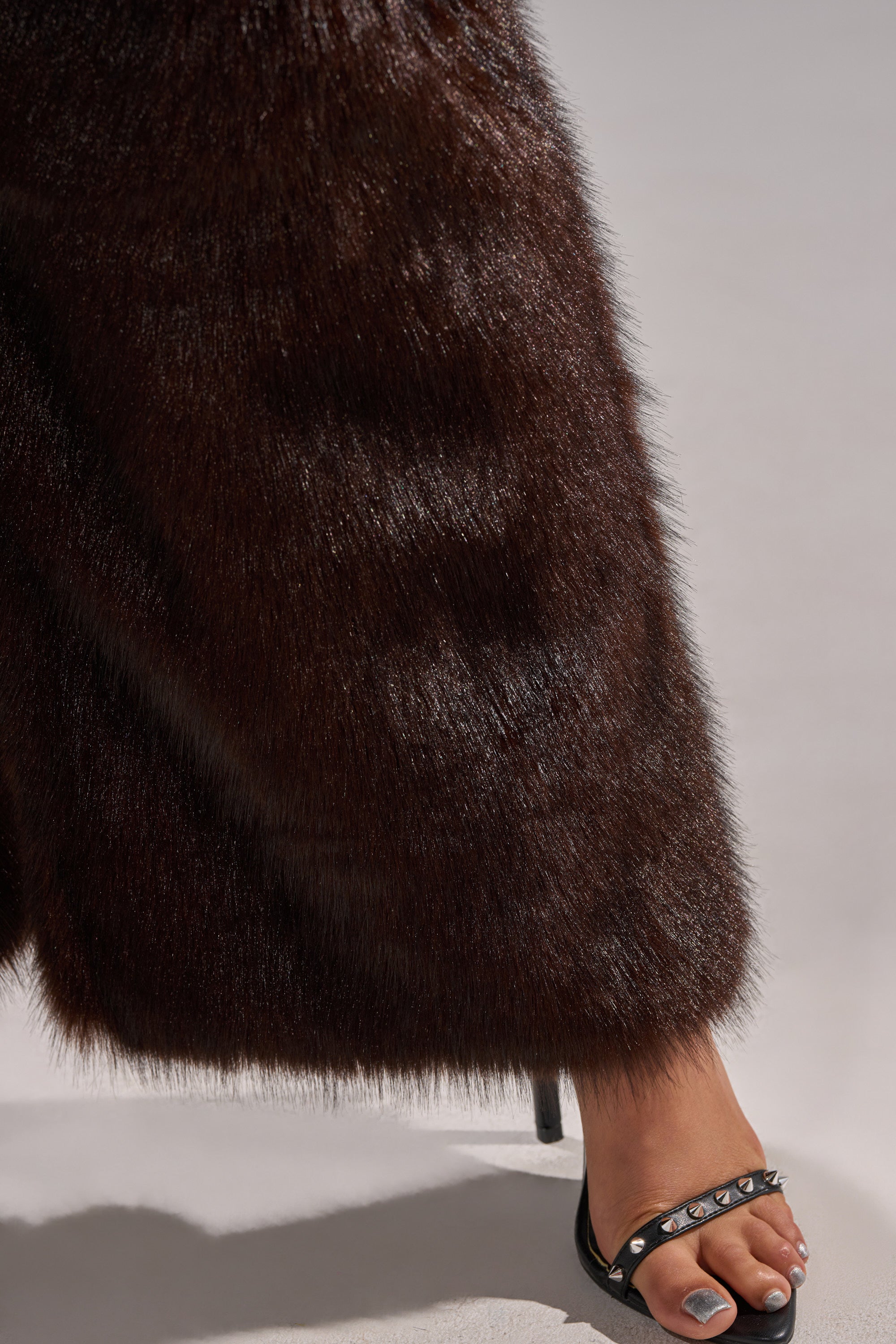 A person wears BOOTS WITH THE FUR WIDE LEG DENIM pants and black heeled sandals with metal studs, showing painted toenails, while standing on a light grey surface.