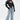 A woman models the WHO KNOWS DISTRESSED WIDE LEG DENIM jeans, paired with a black leather cropped jacket, a corset top, and large hoop earrings; her wet slicked-back hair completes the edgy look.