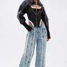 A woman models the WHO KNOWS DISTRESSED WIDE LEG DENIM jeans, paired with a black leather cropped jacket, a corset top, and large hoop earrings; her wet slicked-back hair completes the edgy look.