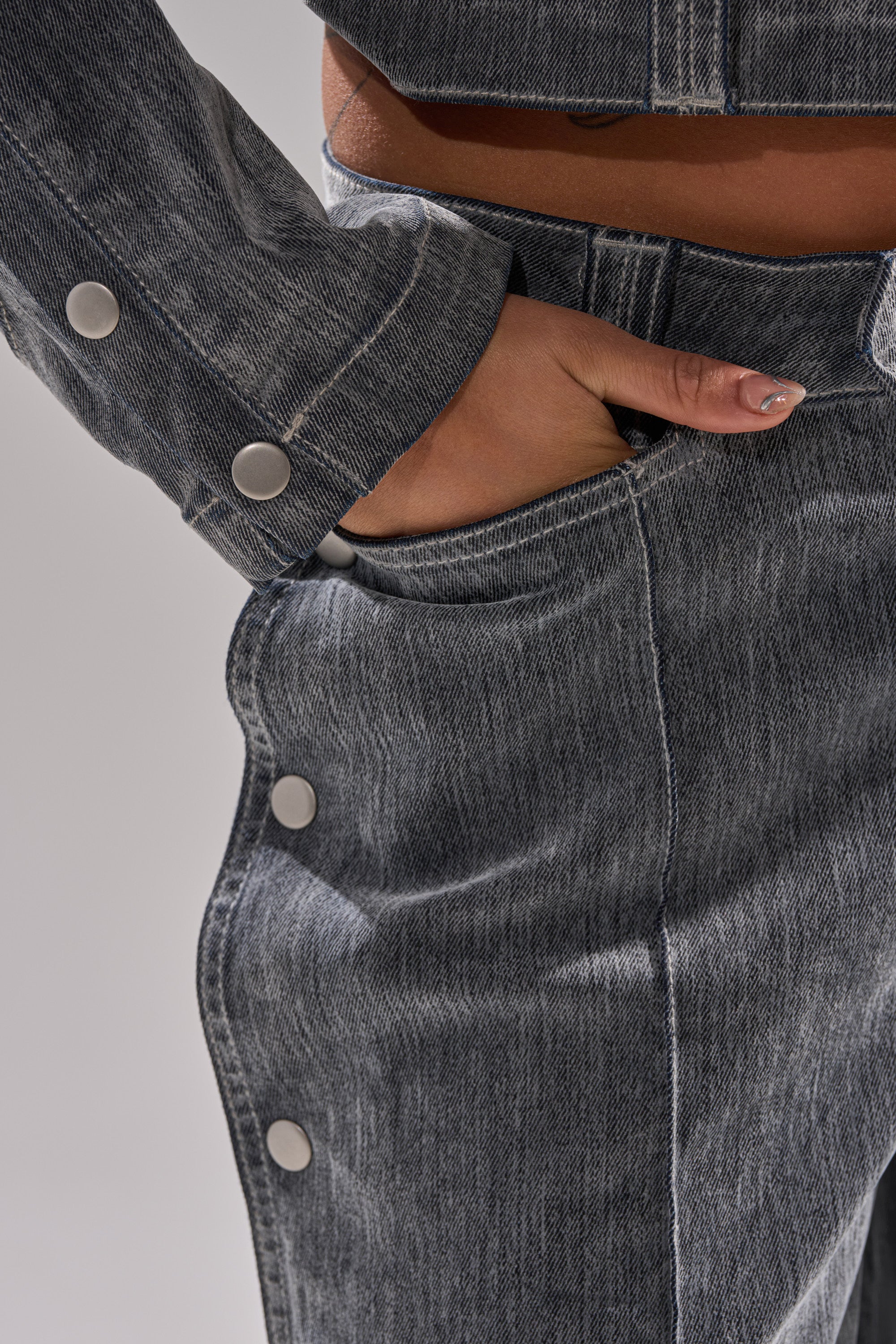 A person wearing CATCHING EYES VELVET DENIM WIDE-LEG PANT with metal snap buttons has their hand partially in the front pocket, showcasing close-up details of the fabric and buttons.