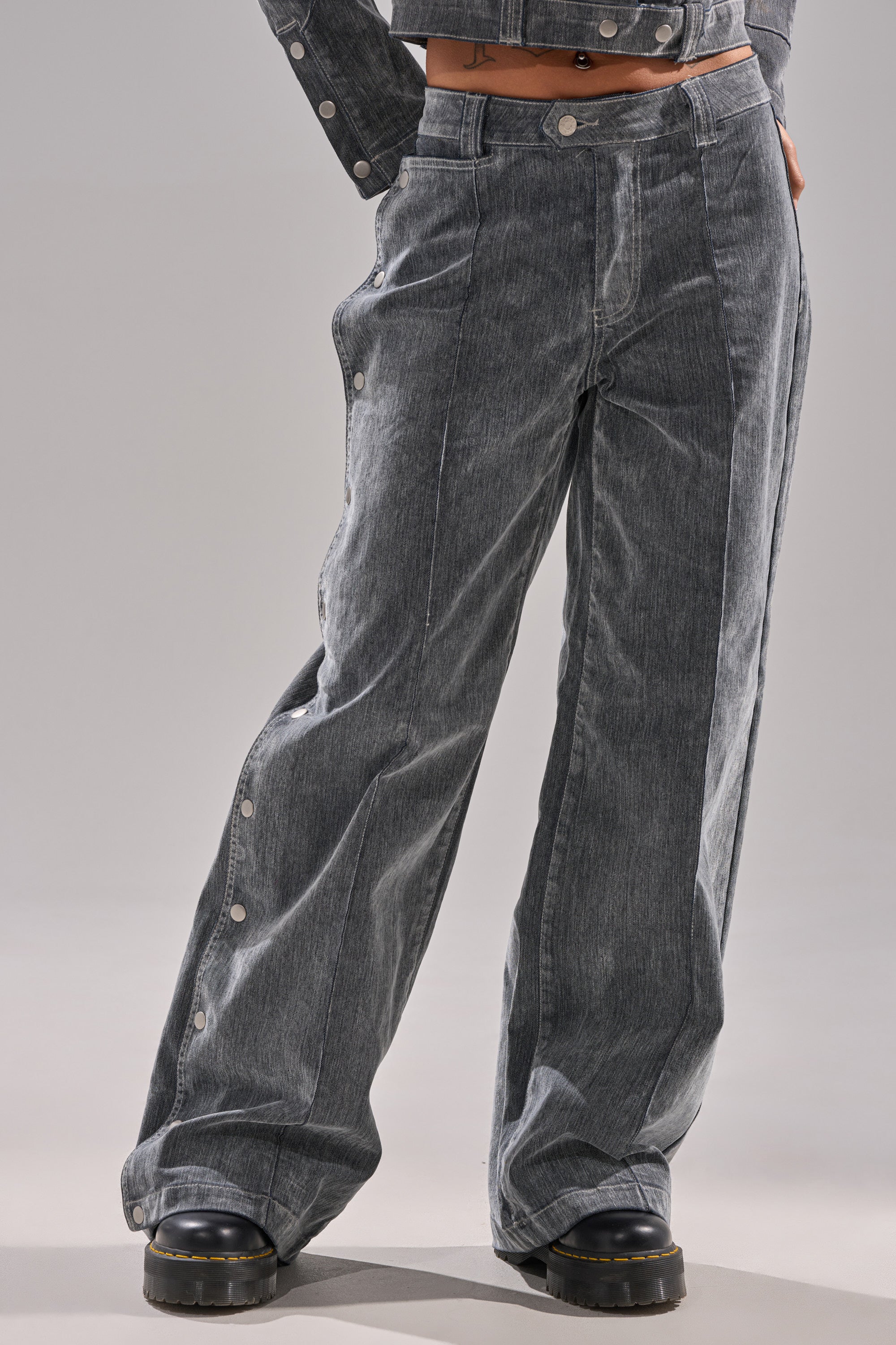 A person models the CATCHING EYES VELVET DENIM WIDE-LEG PANT in faded gray with side snap buttons, styled with black platform shoes against a plain light background.