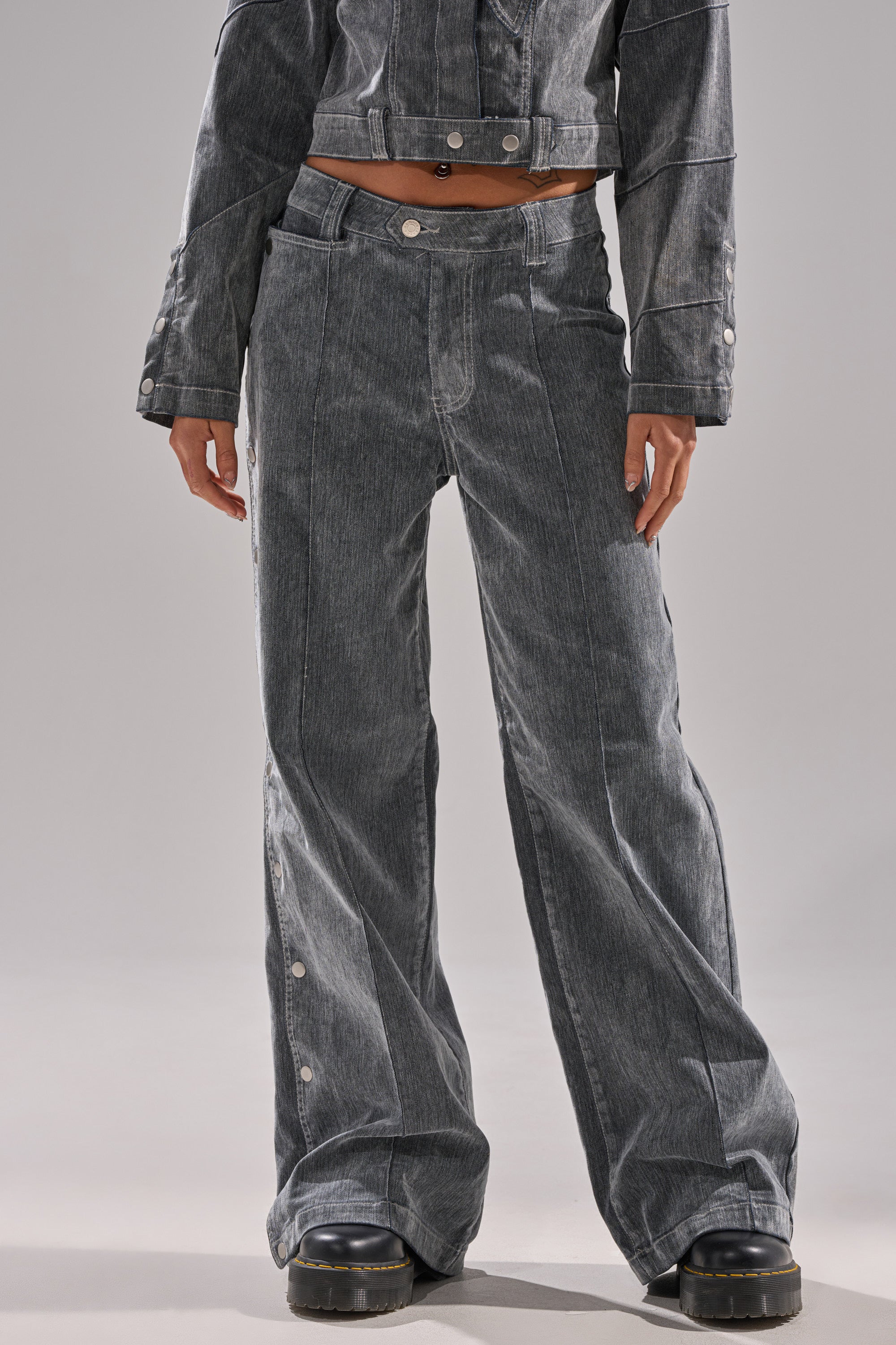 A person is seen from the waist down wearing the CATCHING EYES VELVET DENIM WIDE-LEG PANT in dark gray with side buttons, paired with a matching jacket and black platform shoes.