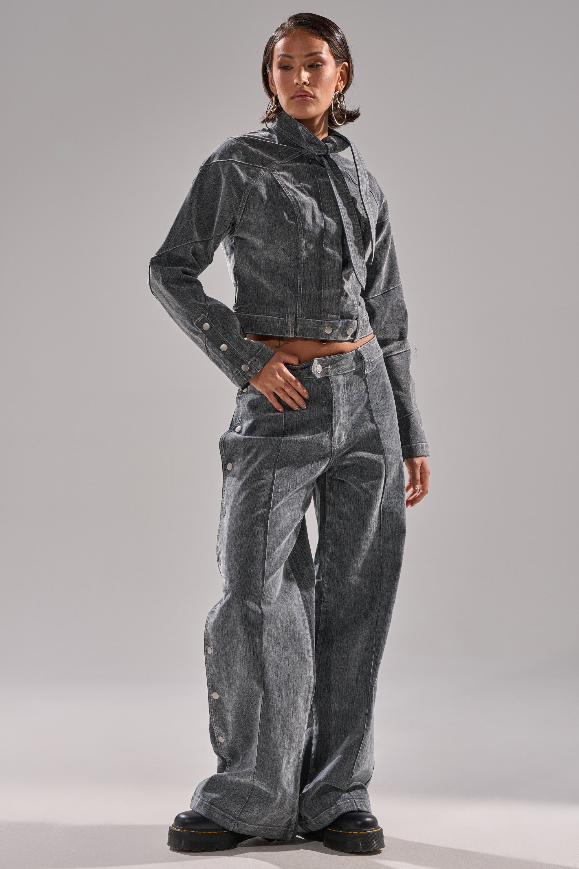 A woman stands with one hand on her hip, wearing CATCHING EYES VELVET DENIM WIDE-LEG PANT in gray, paired with a matching cropped jacket and black platform shoes. The background is plain and light gray.