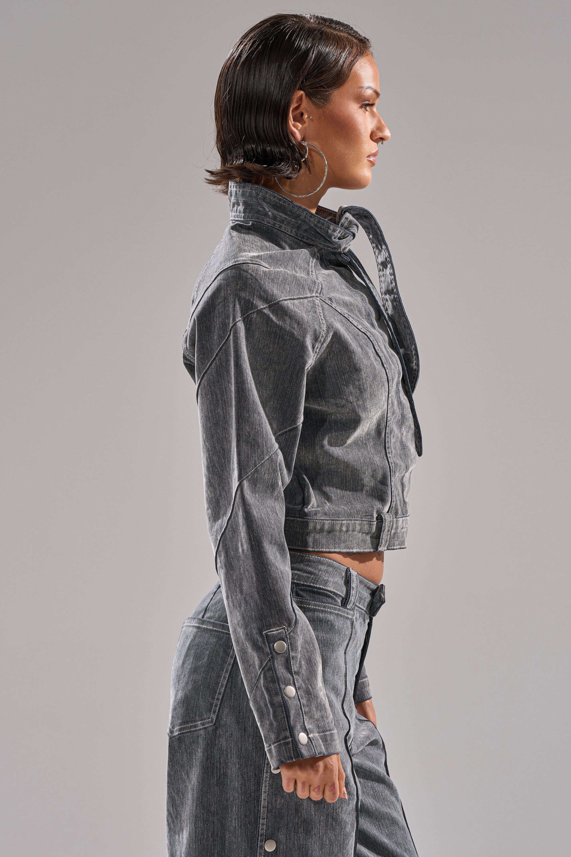 A woman with short dark hair stands in profile against a gray background wearing the CATCHING EYES VELVET DENIM BLOUSE and matching high-waisted pants.